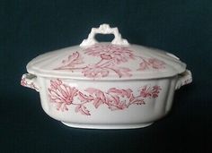 a white casserole with pink flowers on the side and handles, sitting on a black background