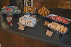 there are several trays of food on the kitchen counter, including bagels and pretzels