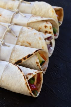 several tortillas wrapped in white paper on a black counter top, with different toppings