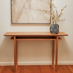 a vase with flowers sitting on top of a wooden table in front of a painting