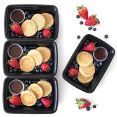 three plastic trays filled with pancakes and berries next to chocolate sauce on the side