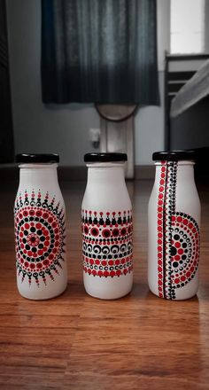 three white vases with designs on them sitting on a wooden floor in front of a window