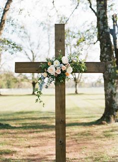 a cross decorated with flowers and greenery in the middle of a grassy area next to trees