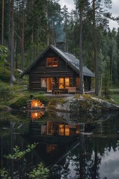 a log cabin is lit up at night by the water's edge in front of it