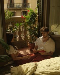 a man and woman are sitting on the floor in front of an open window reading