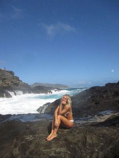 a woman sitting on top of a rock next to the ocean