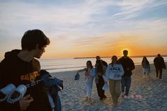 a group of people standing on top of a beach next to the ocean at sunset