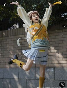 a woman in a yellow shirt and white skirt jumping up into the air with her arms outstretched