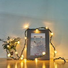 a photo frame with christmas lights around it on a table next to a potted plant