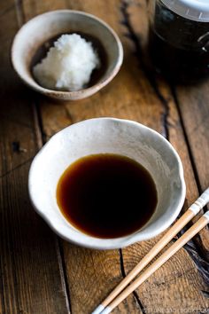 chopsticks and sauce in small bowls on a wooden table next to a mug