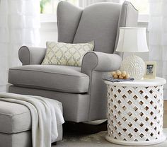 a living room with a chair, ottoman and lamp on the side table in front of a window