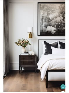 a bedroom with white walls and wood flooring has a painting on the wall above the bed