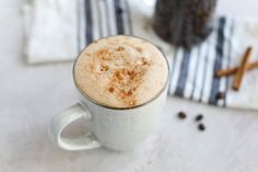 there is a cup of coffee with cinnamon on the table next to some cookies and spices