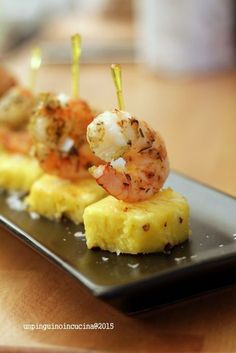 shrimp and pineapple appetizer served on a black plate with toothpicks