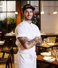 a man in a chef's uniform stands with his arms crossed at the table