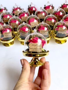 a hand is holding a glass ball with pink flowers in it and there are many other balls behind it