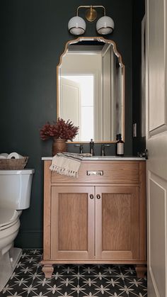 a white toilet sitting next to a bathroom sink under a mirror on top of a wooden cabinet