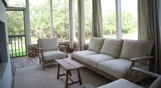 a living room with two couches and chairs next to each other in front of large windows