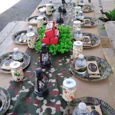 an outdoor table set with plates, cups and utensils in camouflage print cloth