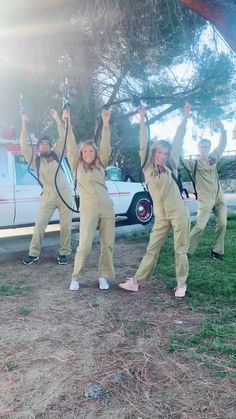 three girls in yellow jumpsuits are holding up their hands while standing under a tree