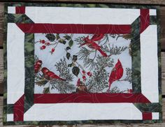 a quilted table runner with red birds and pine needles on it, sitting on a wooden surface