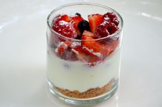 a dessert with strawberries and cream in a glass on a white tableclothed surface