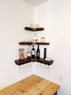 two shelves with wine glasses and bottles on them in a corner room next to a wooden table