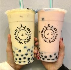 two people holding up drinks in front of a wall with writing on the cups and one has a smiley face drawn on it