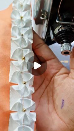 someone is stitching something on the side of a sewing machine with white fabric and gold buttons