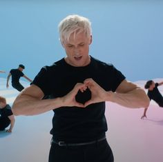 a man making a heart shape with his hands while others are doing yoga exercises in the background