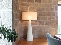 a white lamp sitting on top of a wooden table next to a chair and potted plant