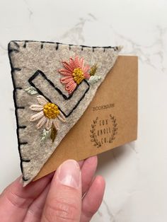 a hand holding a piece of felt with flowers on it and a tag attached to it