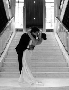 a bride and groom kissing on the stairs at their wedding reception in black and white