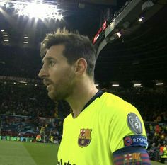 a man in a yellow shirt standing on a soccer field with fans watching from the stands