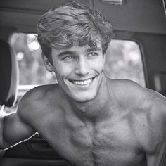 a shirtless man sitting in the back seat of a car smiling at the camera