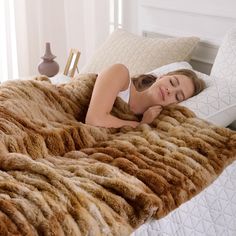 a woman laying in bed under a fluffy brown blanket and she has her eyes closed