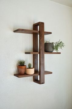 three wooden shelves with plants on them against a white wall in the corner of a room