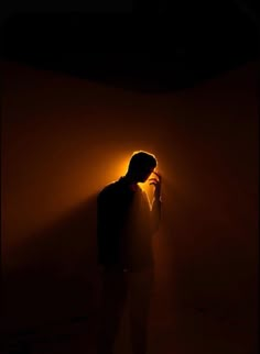 a man standing in the dark holding a cell phone to his ear and looking at it