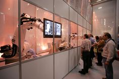 people looking at microscopes on display in a glass walled room with white walls and flooring