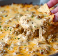 a hand holding a tortilla chip with cheese and ground beef on it in a skillet