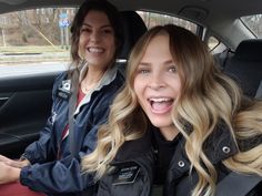 two women sitting in the back seat of a car, one smiling at the camera