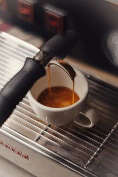 coffee being poured into a white cup on top of a saucer in an oven