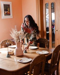 a woman sitting at a wooden table with plates and vases on top of it