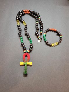 "The \"Rasta Harmony\" Mala Necklace and Bracelet Set is a vibrant and captivating ensemble that combines the essence of Rastafarian culture with the harmonizing energies of Black Wood, Citrine, Red Agate, Malachite, Rasta Beads, and an Ankh pendant. The necklace features round beads made from Black Wood, known for its grounding and protective qualities. The deep black color of the wood creates a strong contrast against the vibrant Rasta Beads, which feature the iconic red, yellow, and green colors associated with Rastafarian culture. These beads symbolize unity, peace, and spiritual growth. Interspersed among the Rasta Beads are Citrine beads, radiating their golden-yellow hues. Citrine is a stone of abundance, joy, and manifestation. It enhances creativity, confidence, and personal power Multicolor Spiritual Bracelets With Black Beads, Spiritual Multicolor Jewelry With Black Beads, Symbolic Multicolor Round Beads Jewelry, Beaded Jewelry Inspiration, Rastafarian Culture, Ankh Pendant, Necklace And Bracelet Set, Citrine Beads, Mala Bracelet