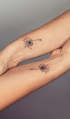 two people with matching tattoos on their arms holding each other's hands and one has a dandelion tattoo