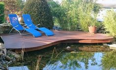 two lawn chairs sitting on top of a wooden deck next to a small pond in a garden