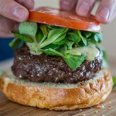 a hamburger with lettuce and tomato being held up by someone's hand