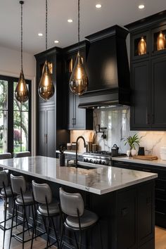 a large kitchen with black cabinets and marble counter tops, hanging lights over the island