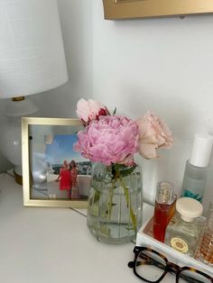 pink flowers in a vase on a white desk next to a framed photograph and eyeglasses