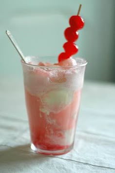 a drink with cherries on the top and ice in a tall glass sitting on a table